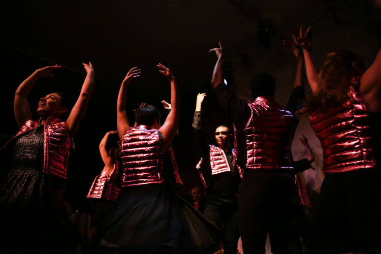 Several figures wearing metallic pink vests with arms upraised against a dark background